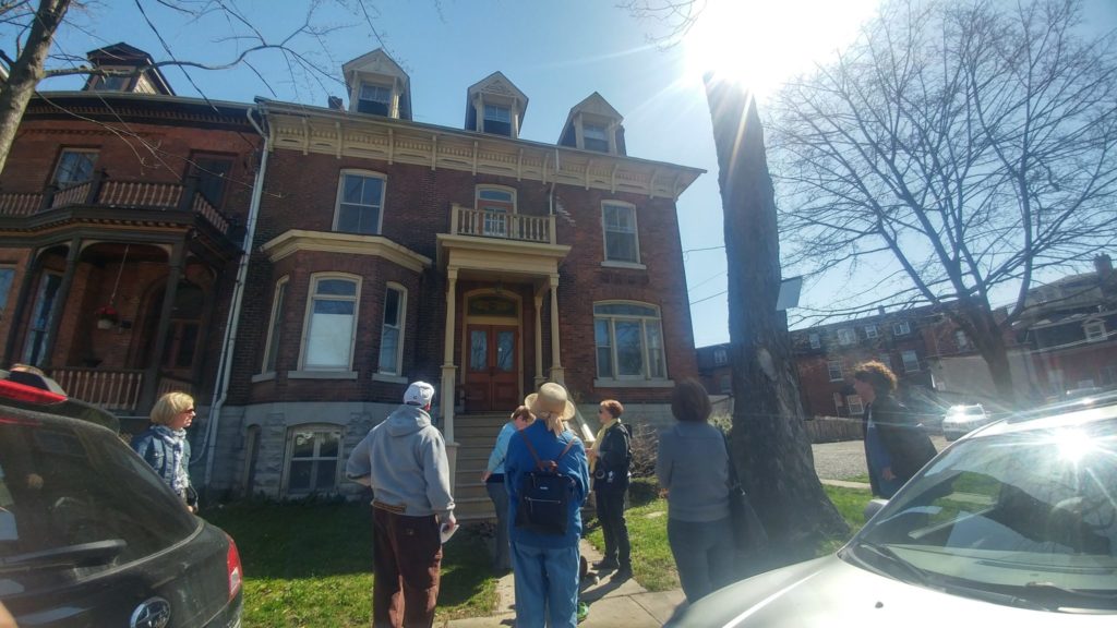 Six individuals are visible in the foreground staring up at a 2.5 story brick heritage house at 55 West Street at Stop 4A on the tour.